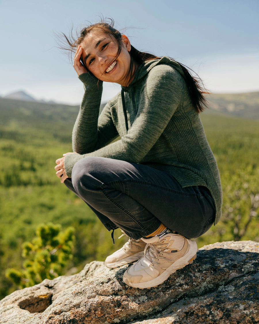 Three-quarter view of women’s eucalyptus alpaca hoodie showing ribbed side panels and thumbhole cuffs on a model outdoors