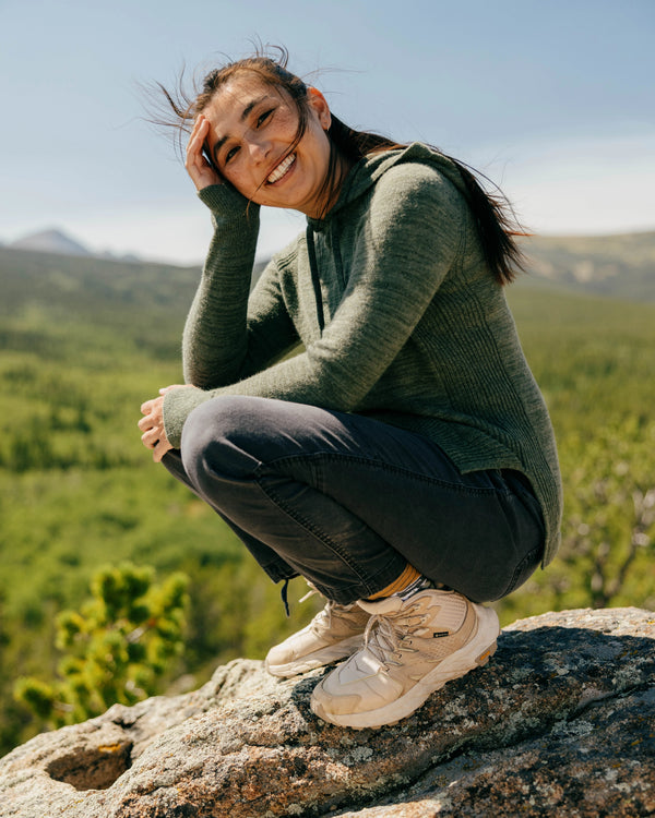 Three-quarter view of women’s eucalyptus alpaca hoodie showing ribbed side panels and thumbhole cuffs on a model outdoors