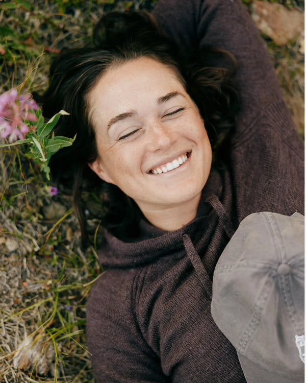 Woman lying on grass smiling in a fig alpaca hoodie relaxed outdoor setting