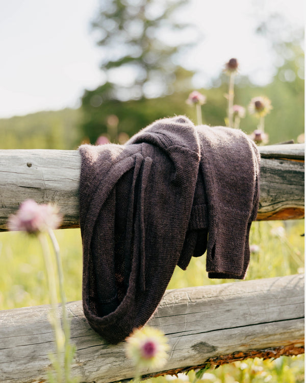 Women’s alpaca hoodie draped over a wooden fence in a sunlit meadow