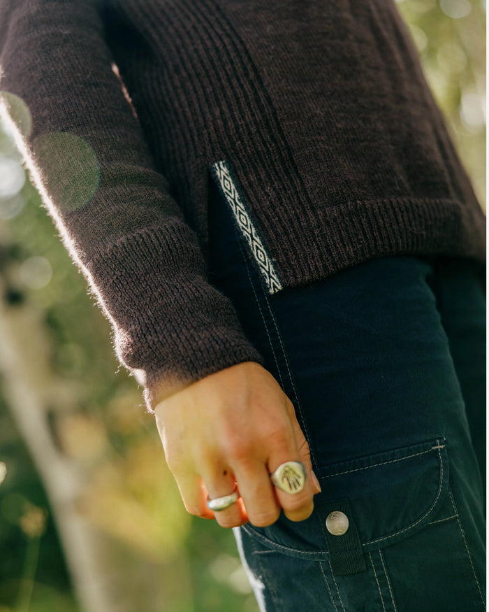 Side view of women’s alpaca hoodie in fig showing ribbed knit, side hem slit with patterned tag on model outdoors