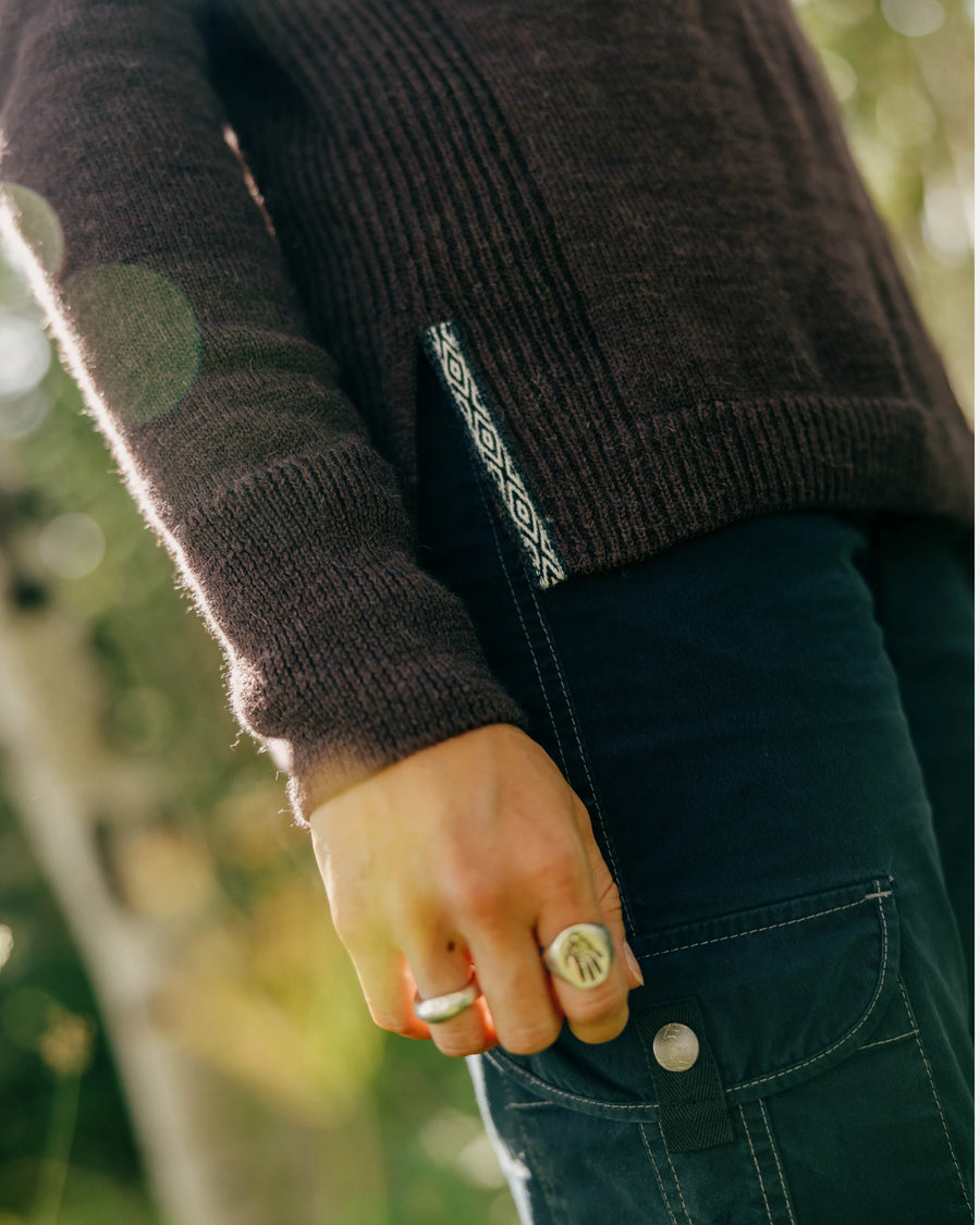 Side view of women’s alpaca hoodie in fig showing ribbed knit, side hem slit with patterned tag on model outdoors