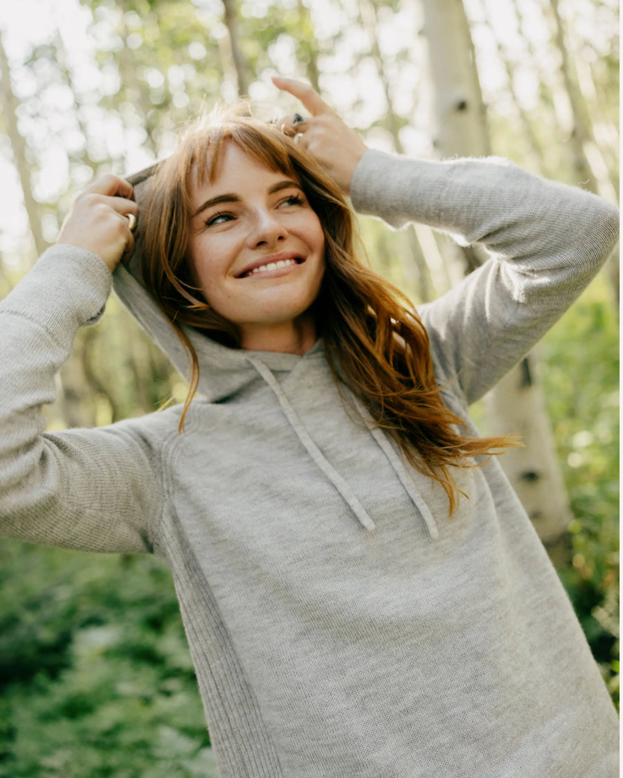 Front view of women’s alpaca hoodie showing drawstring hood, ribbed side panels, and relaxed fit with sunlit forest background