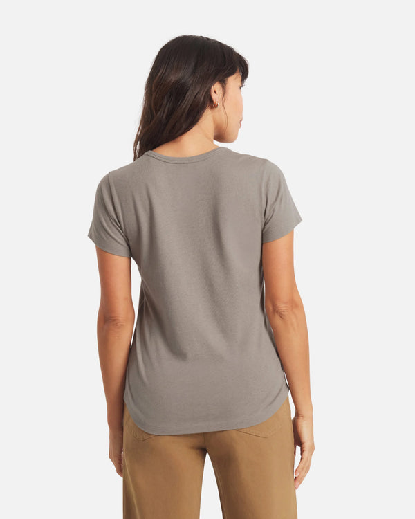 Back view of Women’s Essential Tee in Stone, regular fit with short sleeves and curved hem on model against light background