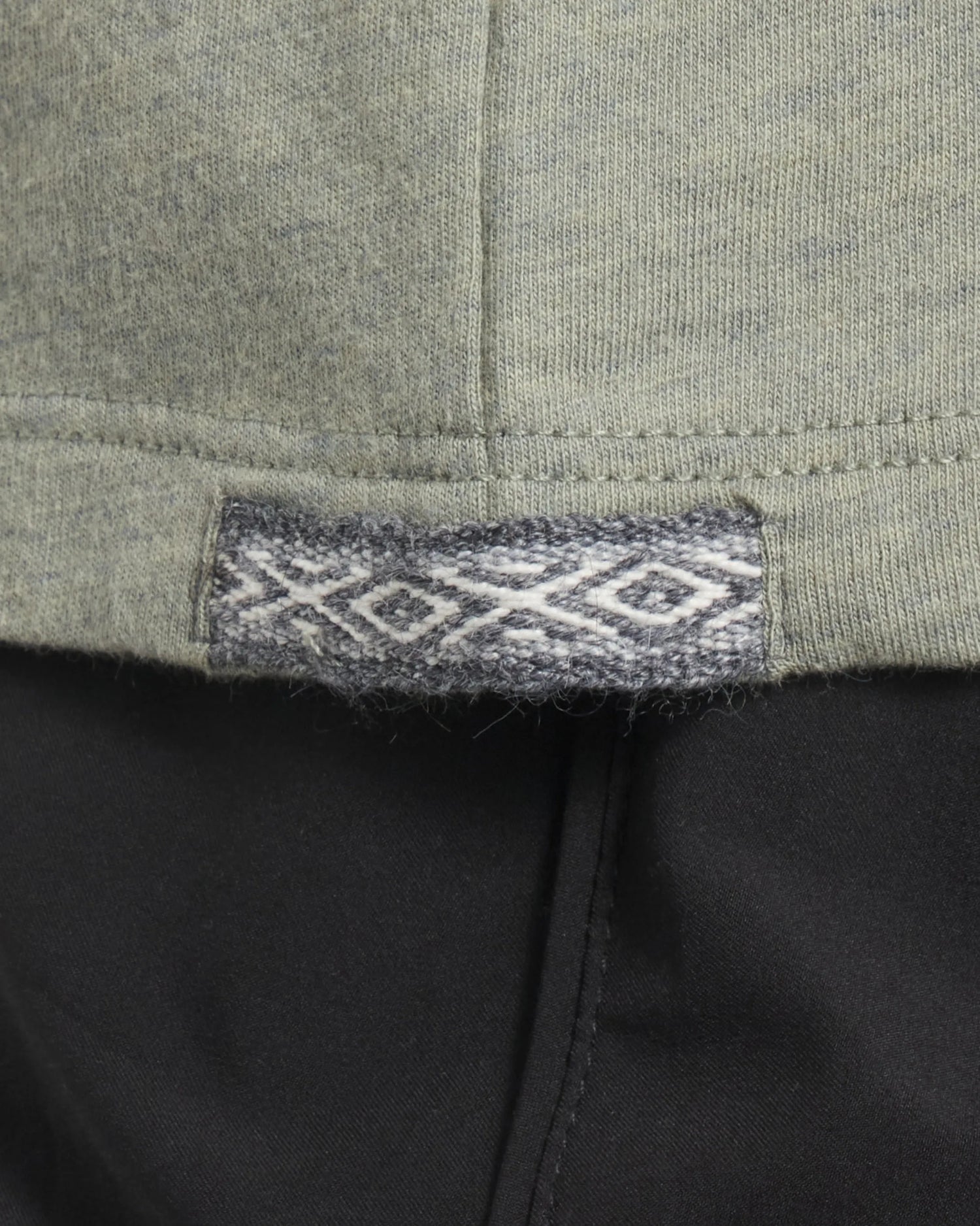 Close-up of Women’s Essential V-neck hem in Balsam showing woven Inca ID label and side seam over black pants