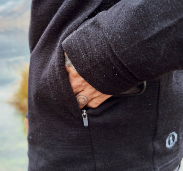 Close-up side view of Breathe Zip Hoodie showing zippered side pocket with hand and phone, blurred outdoor background