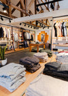 Boutique interior showing folded alpaca sweaters on a central table, wooden clothing racks, and warm lighting
