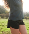 Person wearing charcoal T-shirt and black athletic shorts standing in a sunlit grassy field