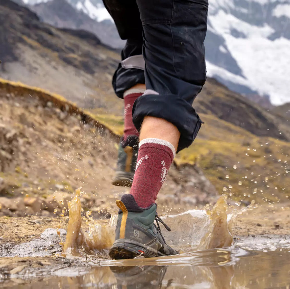 Hiker splashing through a muddy mountain puddle wearing maroon Thermal Condór crew socks