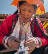 Quechua woman handweaving colorful bracelets while wearing traditional Andean clothing