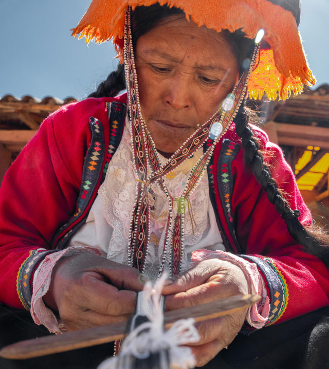 Quechua woman handweaving colorful bracelets while wearing traditional Andean clothing