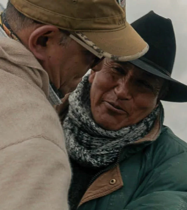 Two men embracing outdoors, both wearing hats, jackets, and a knit scarf