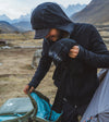 Man wearing a black zip hoodie packing a backpack at a mountain campsite