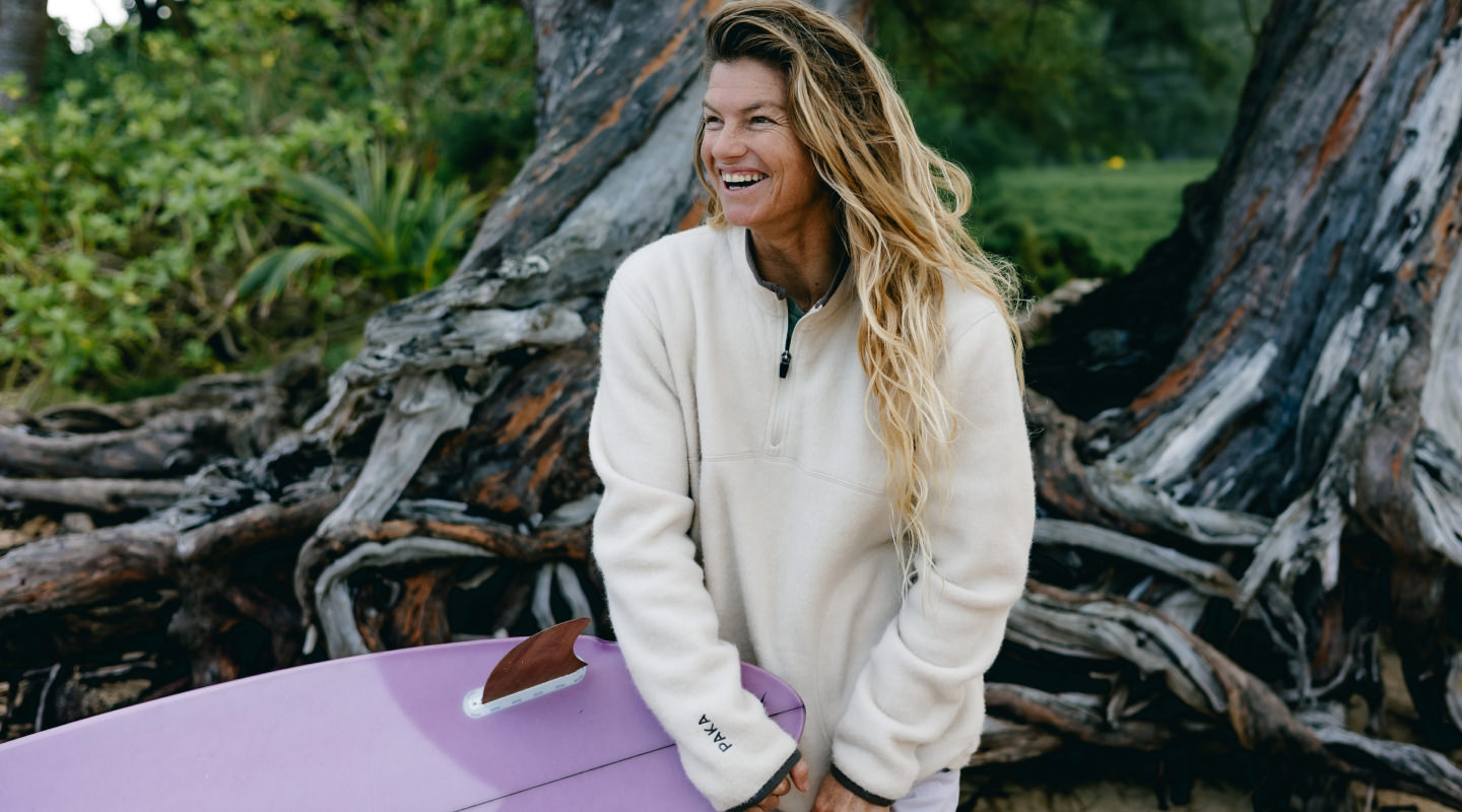 Model wearing cream PAKACLOUD alpaca fleece jacket standing on rocks in a forest setting