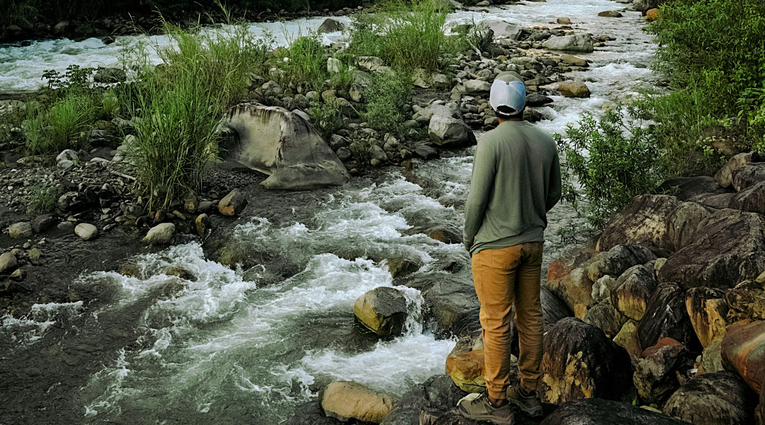 Hiker in yellow jacket standing on a rock beside a mountain stream in a green forest