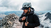 Hiker adjusting the hood of a black insulated jacket on a snowy mountain ridge