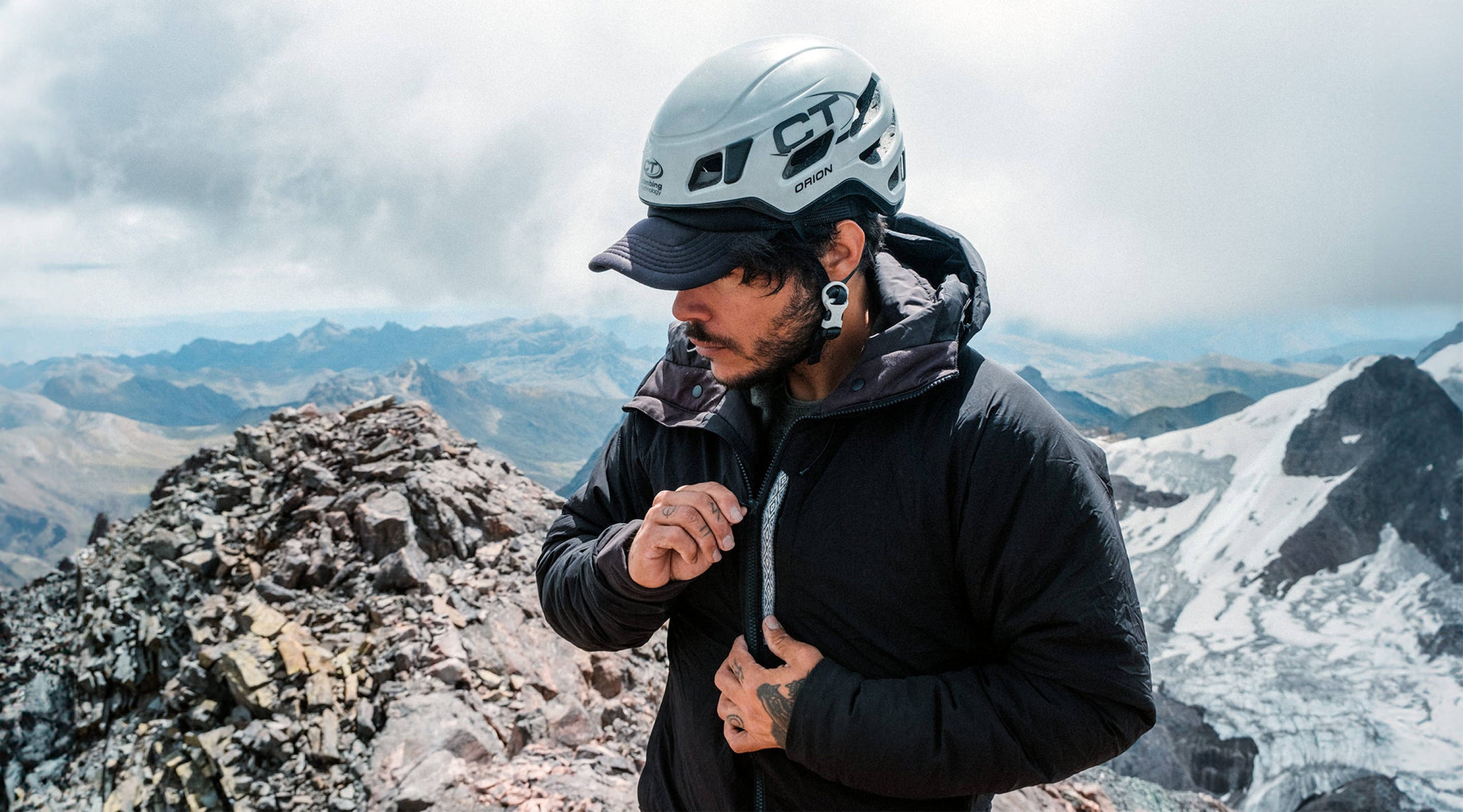 Hiker adjusting the hood of a black insulated jacket on a snowy mountain ridge
