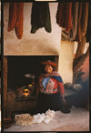 Quechua woman in traditional dress sitting by a hearth in a rustic room with hanging handwoven textiles and raw wool
