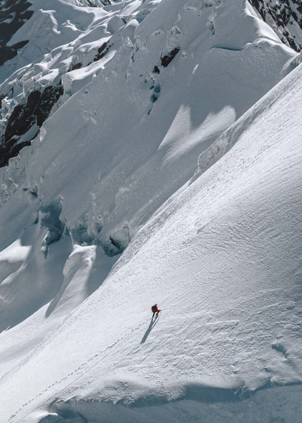 Solo climber in a red puffer jacket ascending a steep snow-covered mountain slope