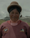 Smiling woman in traditional Andean clothing standing outdoors with mountains in the background
