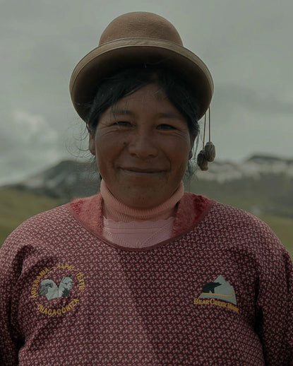 Smiling woman in traditional Andean clothing standing outdoors with mountains in the background