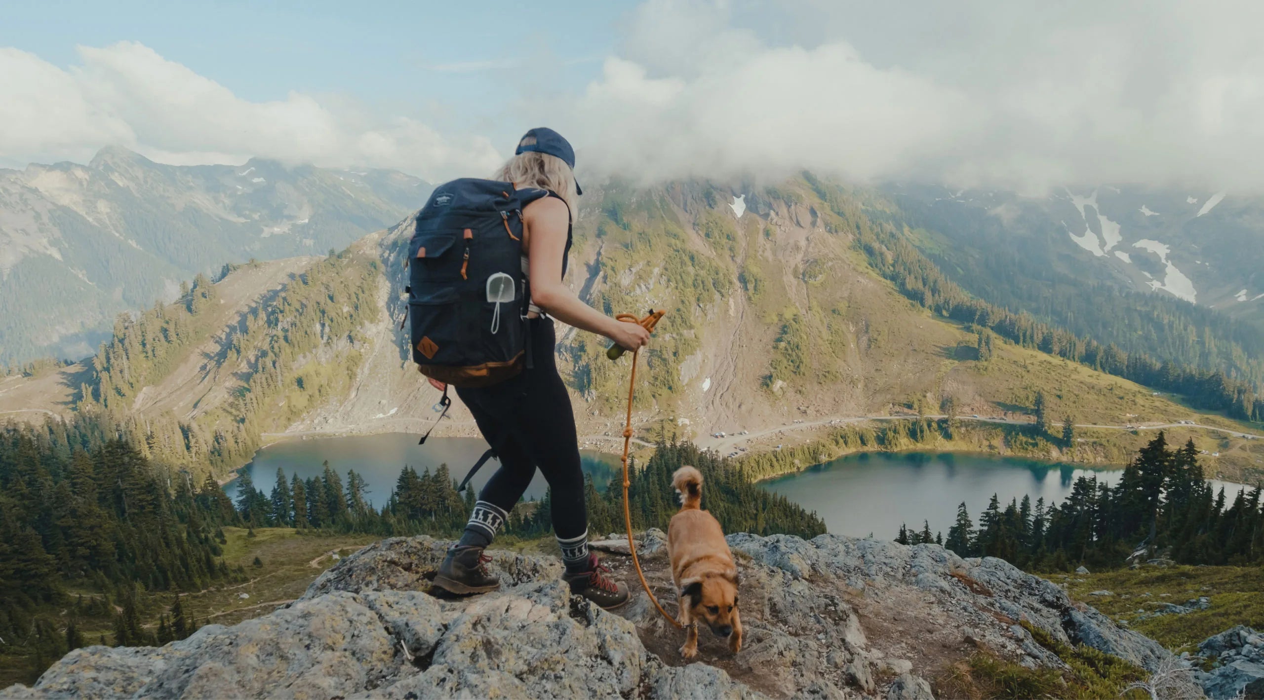 A woman hiking with her dog in a beautiful landscape of mountains, pines and a lake 