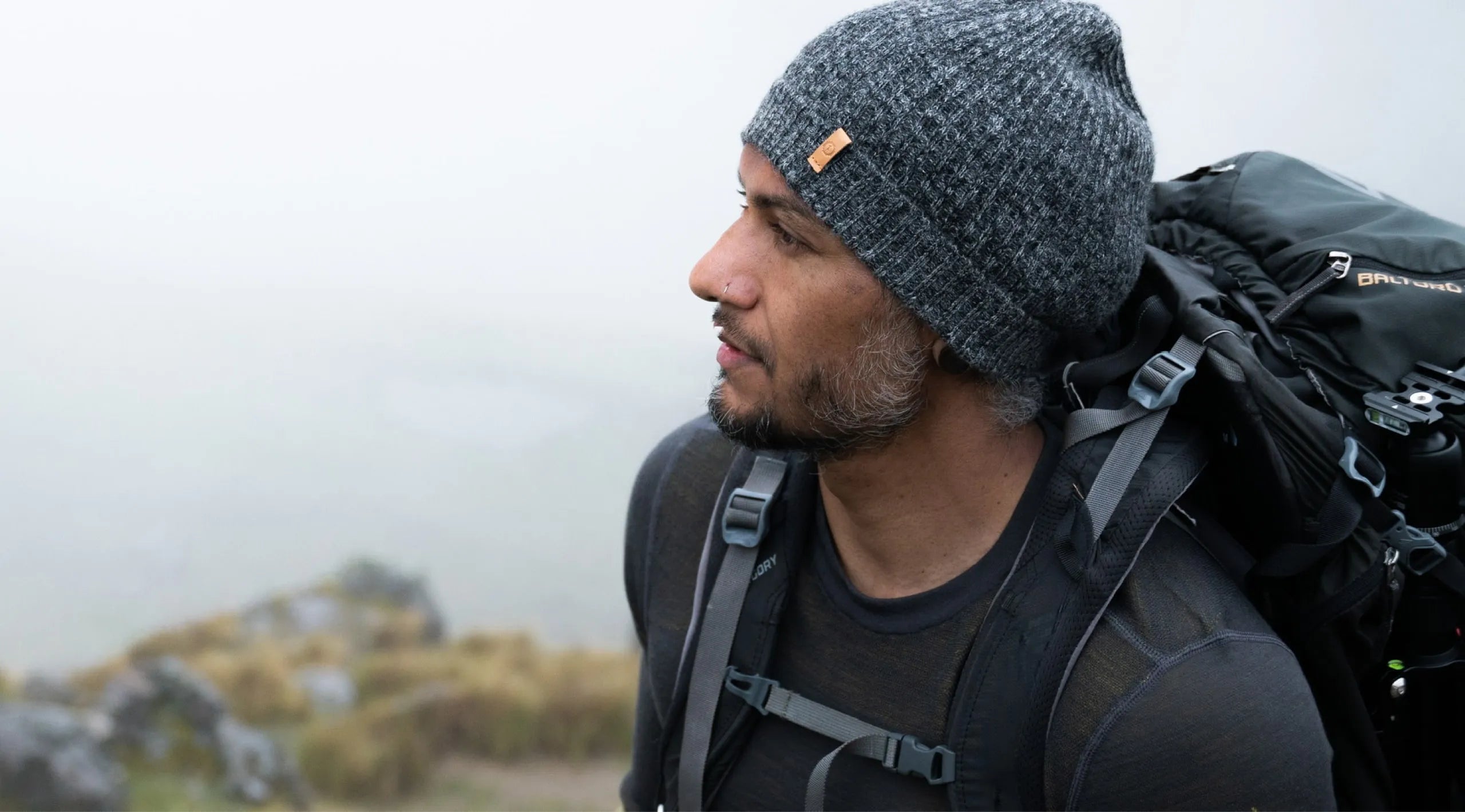 A backpacker wearing a charcoal alpaca beanie in a cloudy place