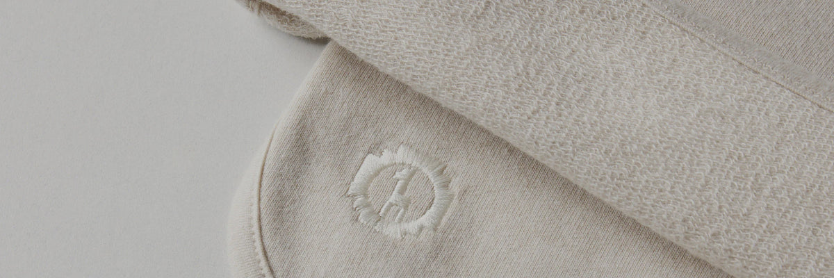 Close-up of Tri-Blend Terry fabric showing soft looped terry texture and small embroidered PAKA logo on a neutral cream background