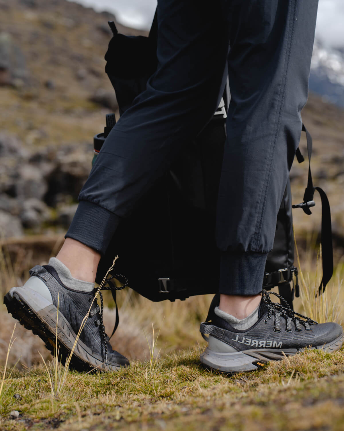 Hiker’s lower legs wearing light gray alpaca ankle socks and gray trail shoes on a grassy mountain trail