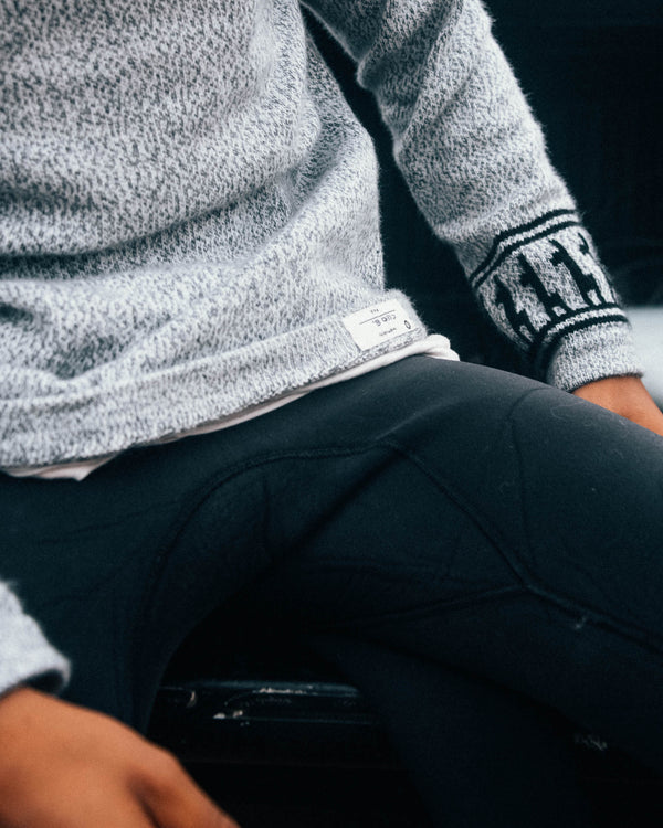 Seated close up of The Costa light grey crewneck sweater showing marled knit, ribbed side panels, and patterned sleeve cuff