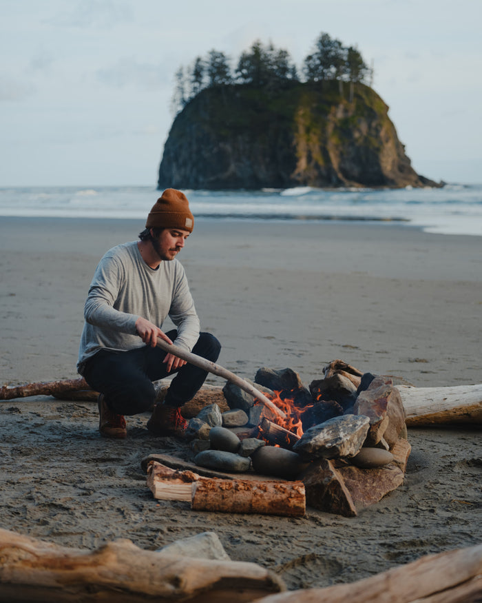 Model Tending Campfire on Beach in Men’s Heather Grey Aire Long Sleeve Outdoor Shirt – PAKA Apparel