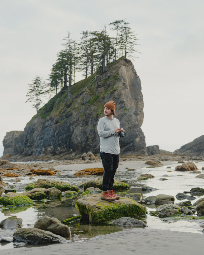 Man on Coast with Camera in Front of Large Rock Formation in Heather Grey Aire Long Sleeve Shirt – PAKA Apparel