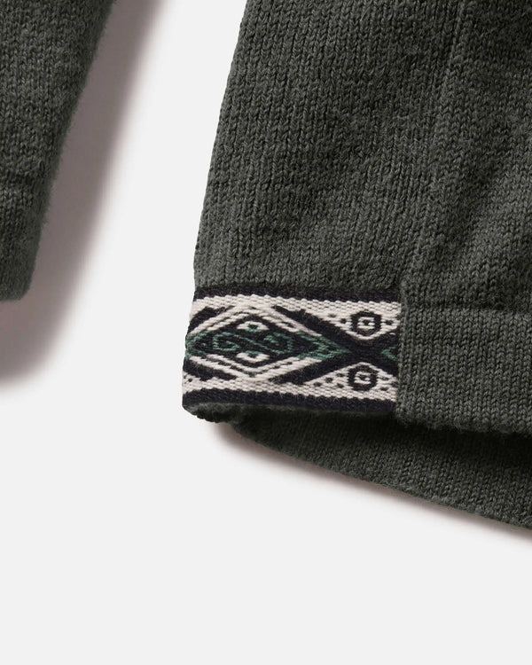 Close-up of The Hoodie sleeve cuff showcasing geometric woven trim on moss green alpaca knit fabric against a white background