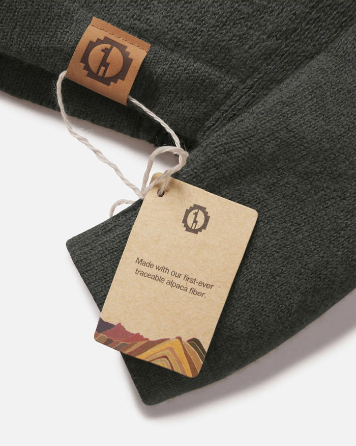 Close-up of The Hoodie sleeve with kraft tag reading Made with our first-ever traceable alpaca fiber and leather logo tab