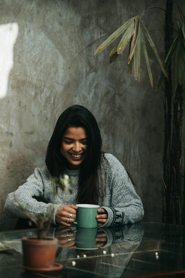 Woman Model laughing and drinking coffee wearing the Costa alpaca sweater by Paka Apparel