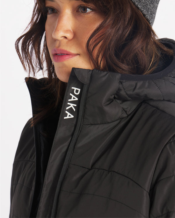 Close-up three-quarter view of Women’s PAKAFILL Midweight Puffer on model, showing PAKA logo on front placket and quilted black insulation on white background