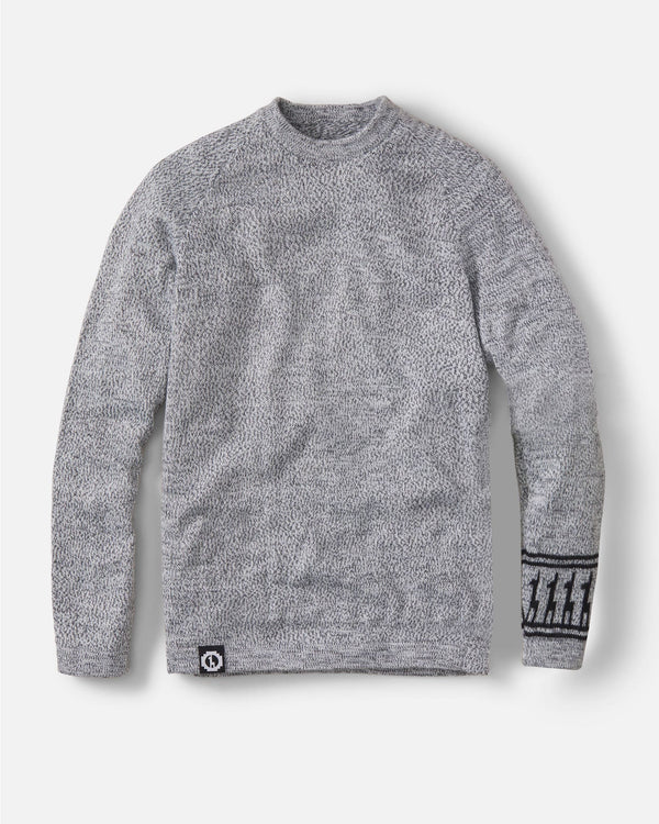 Front view of The Costa sweater showing gray sherpa fleece texture, patterned cuff, and logo patch on light background