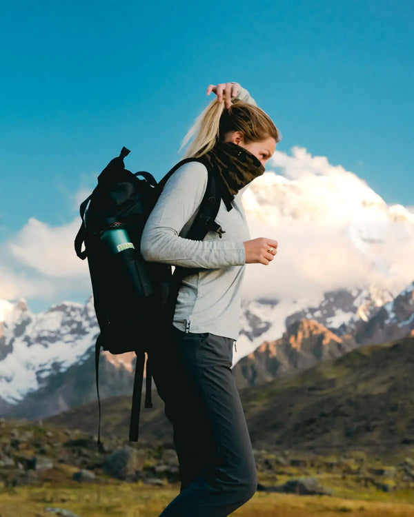 Side view of Women’s Aire long sleeve shirt in heather grey on model, slim fit with neck gaiter and backpack in mountains